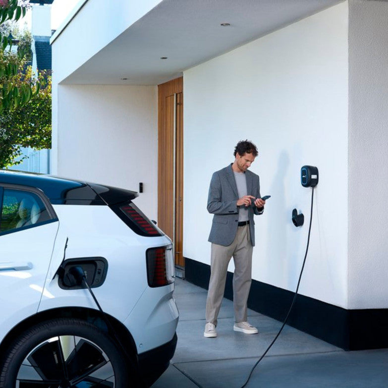Voiture électrique blanche branchée à une Wallbox près d’une maison.